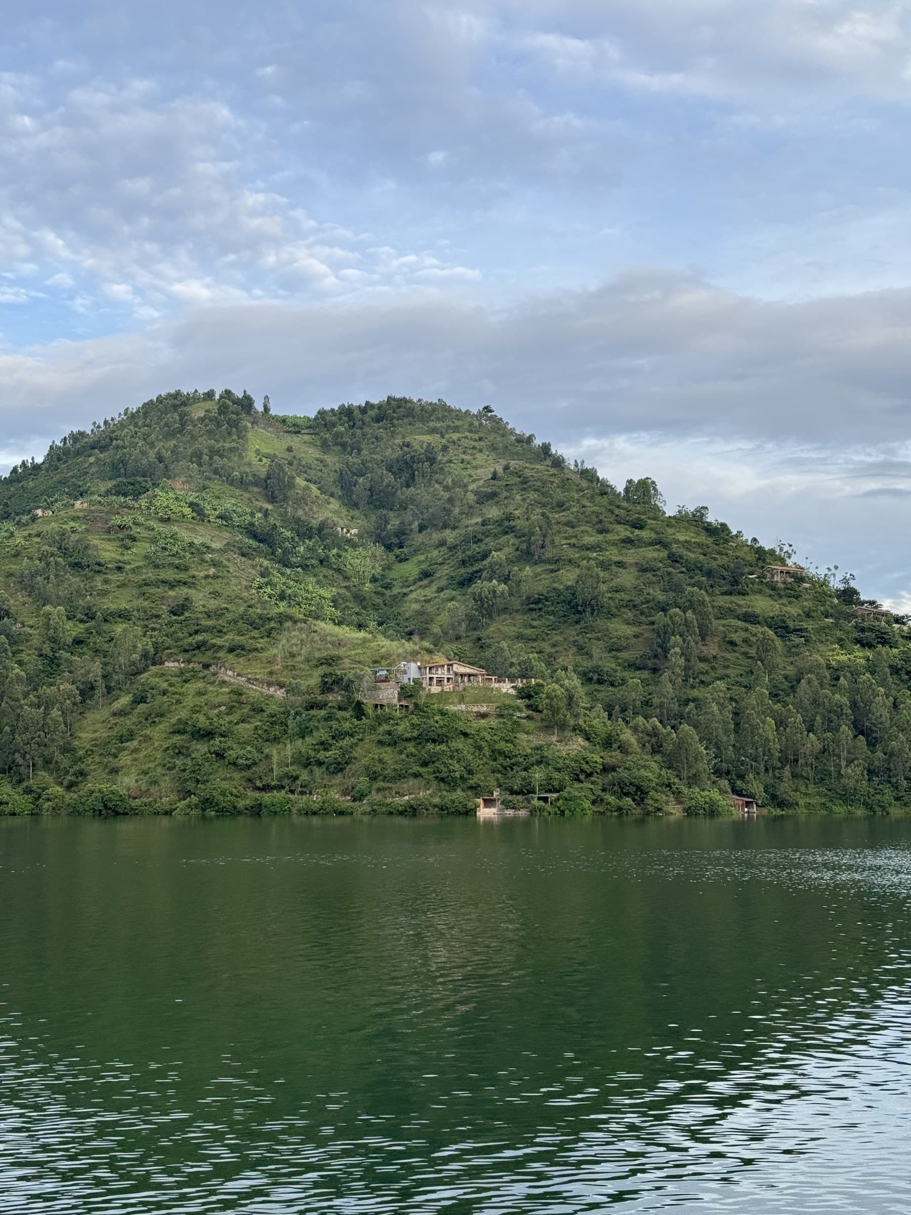 A lakeside home on a green Rwandan hillside above calm water at dusk